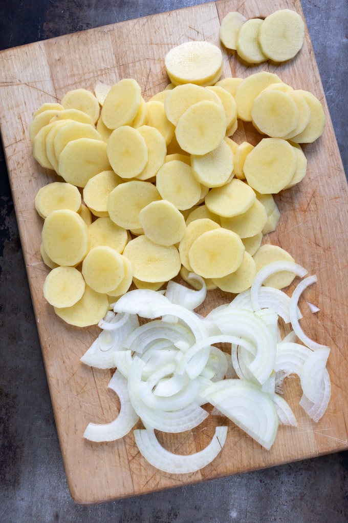 Sliced potatoes and onions on a cutting board.