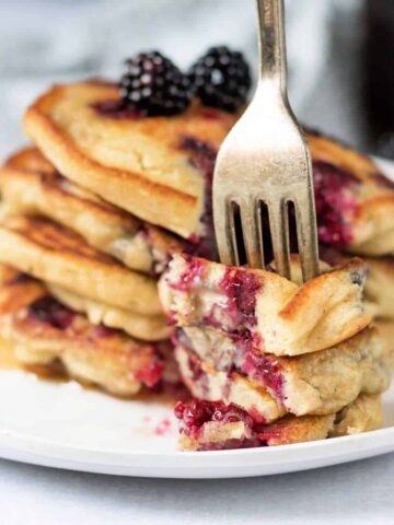 Stack of pancakes with blackberries and a fork in a piece..