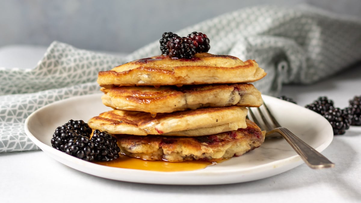 Stack of pancakes with blackberries and maple syrup.