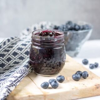 Jar of blueberry compote on a wooden board.