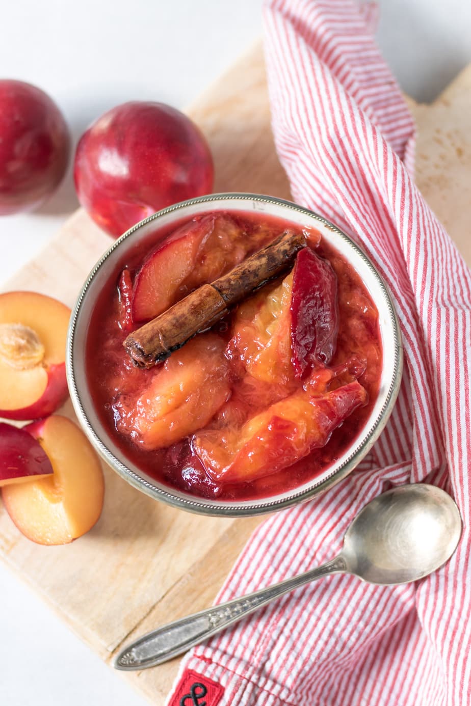 Bowl of cooked plums with cinnamon stick.