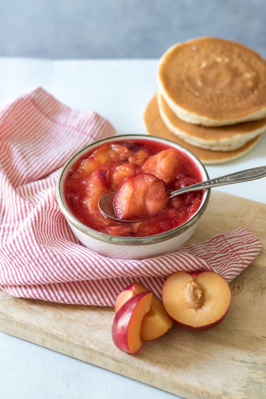 Bowl of plum compote next to pancakes.