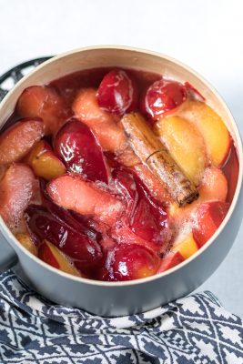 Pot of cooked plums with cinnamon stick.