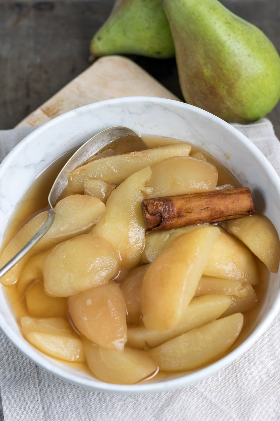Close up of a bowl of stewed pears with a cinnamon stick and a serving spoon.