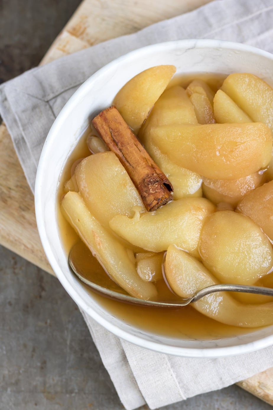 Close up of a bowl with cooked pears in cinnamon syrup with a cinnamon stick.