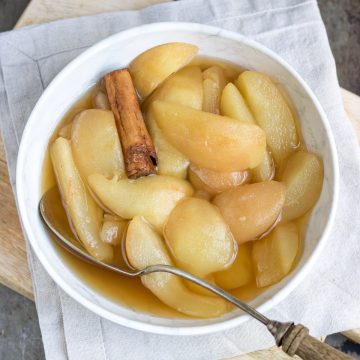 Bowl of stewed pears with a serving spoon and a cinnamon stick.