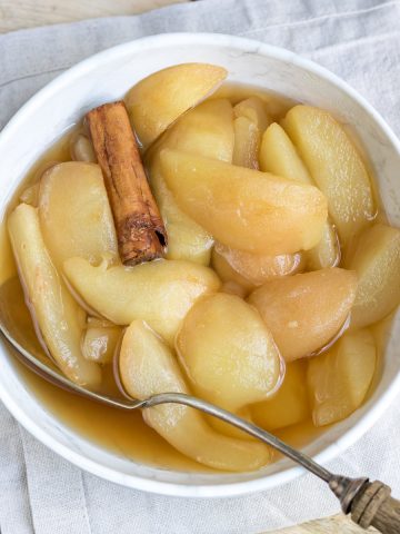 Bowl of stewed pears with a serving spoon and a cinnamon stick.