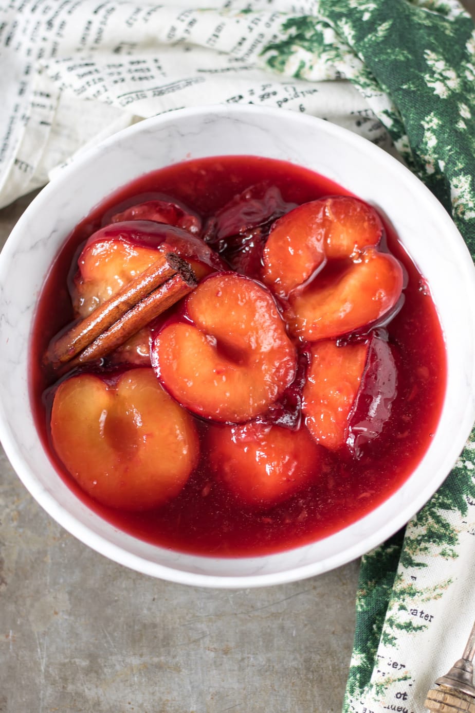 Bowl of cooked plums and a cinnamon stick.