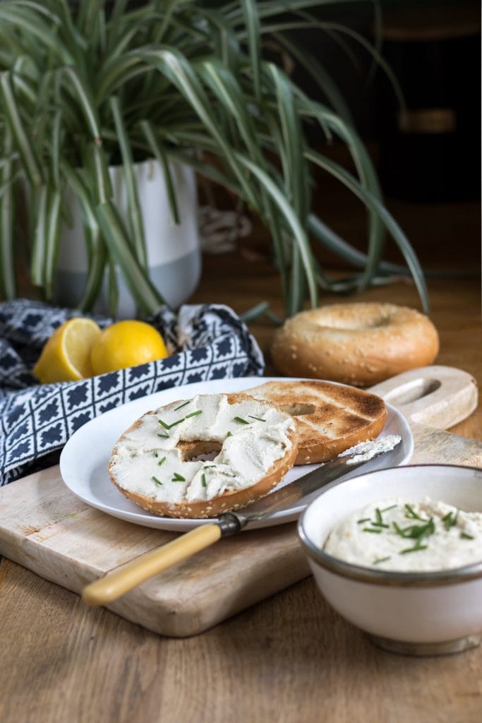 Plate of soft cheese on bagels next to a plant.