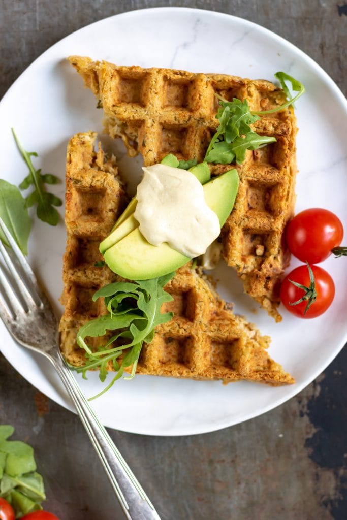 Waffled falafel on a plate with avocado, tomatoes and hummus.