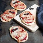 Pita pizzas decorated like Halloween mummys on a table and wooden board.