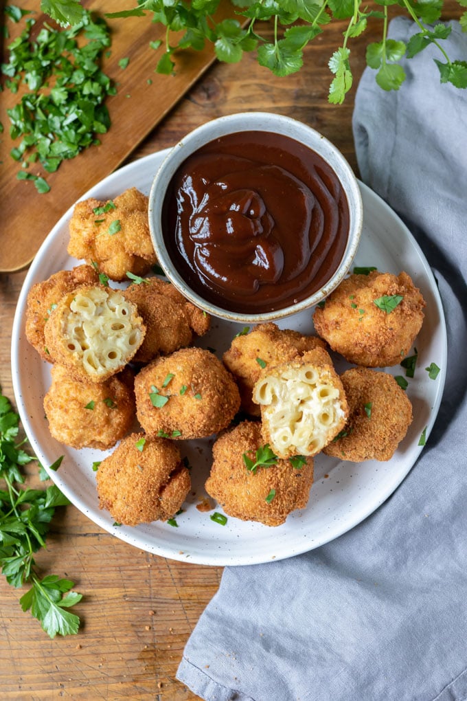 Plate of macaroni cheese balls, with bbq dip and two balls cut open.