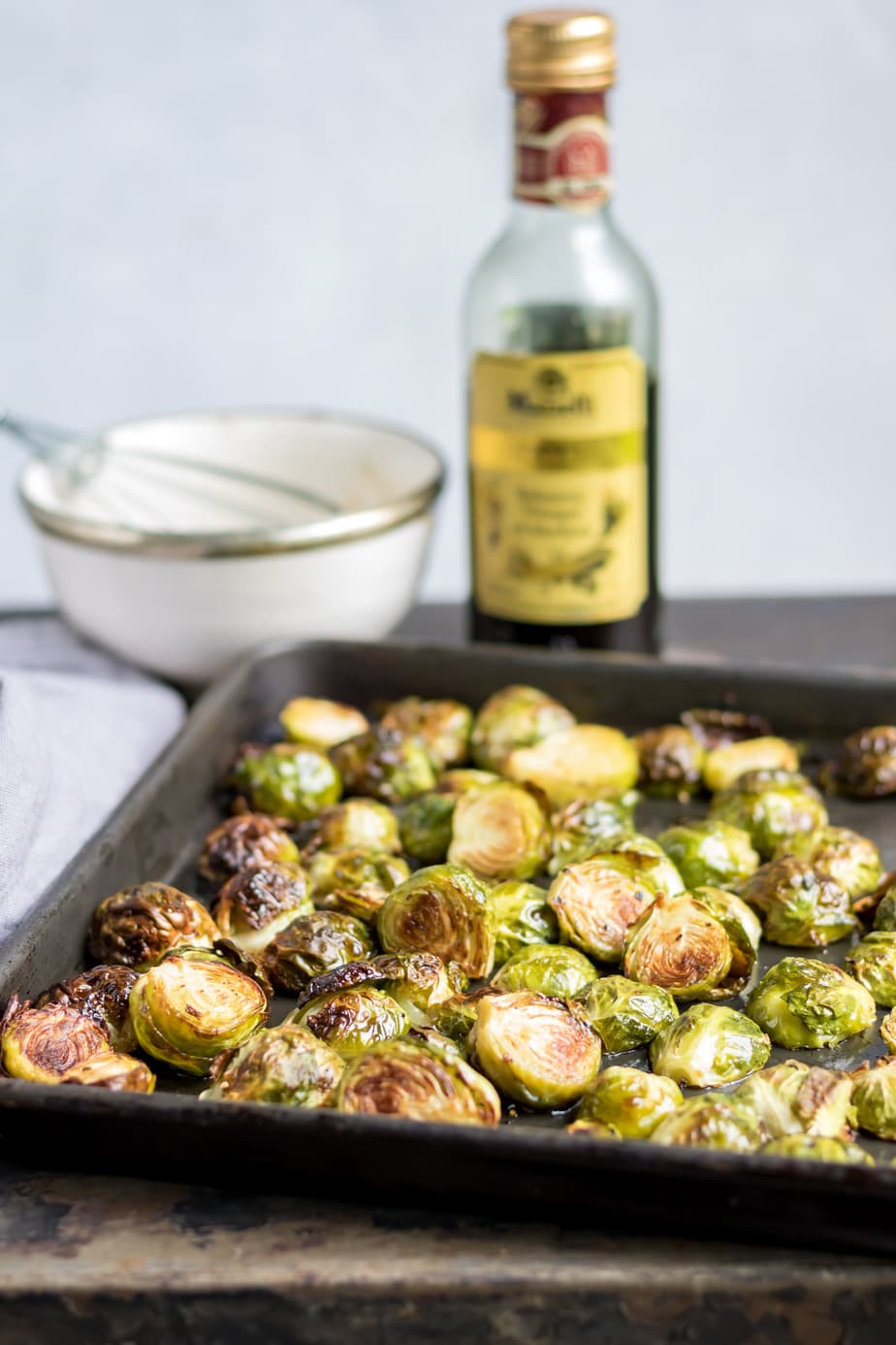Tray of roasted sprouts in front of bottle of balsamic vinegar.