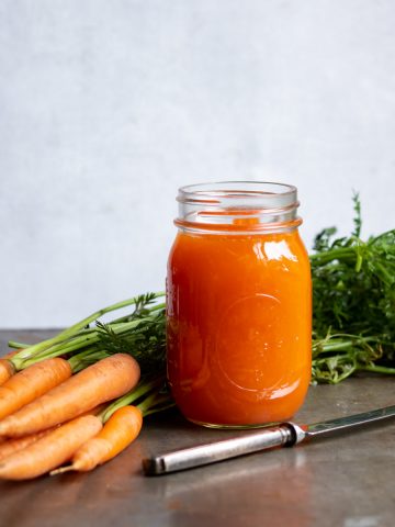 A jar of carrot jam next to a knife and carrots.