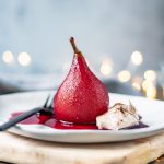 Red wine poached pear on a plate with cinnamon cream.