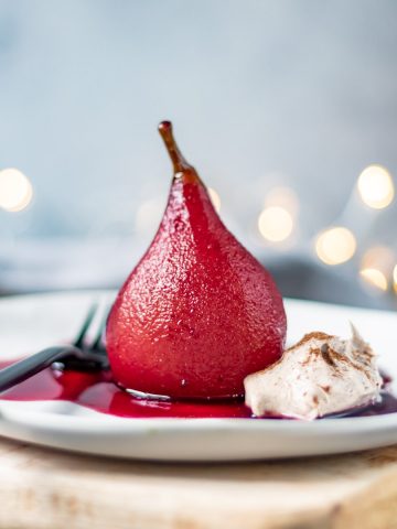 Red wine poached pear on a plate with cinnamon cream.