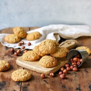 Cookies on a wooden board next to a knocked over container of hazelnuts.