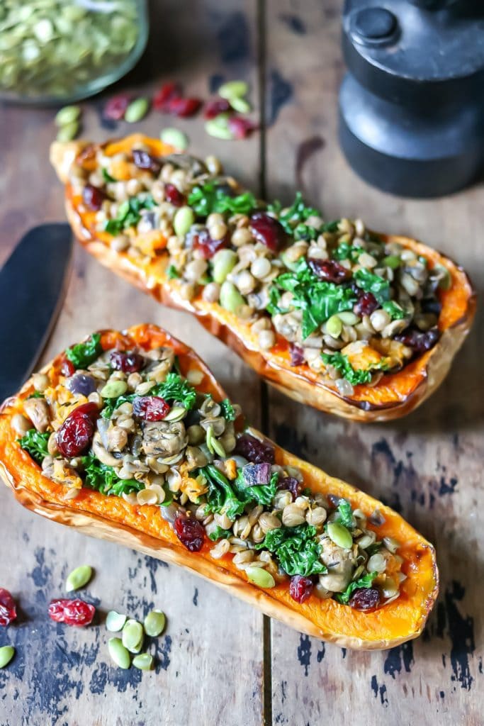 Two stuffed squash halves with lentils and kale on a table.