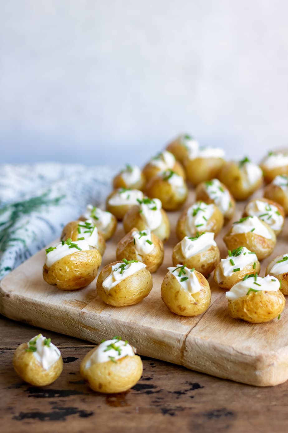 Rows of mini baked potatoes with sour cream on a board.