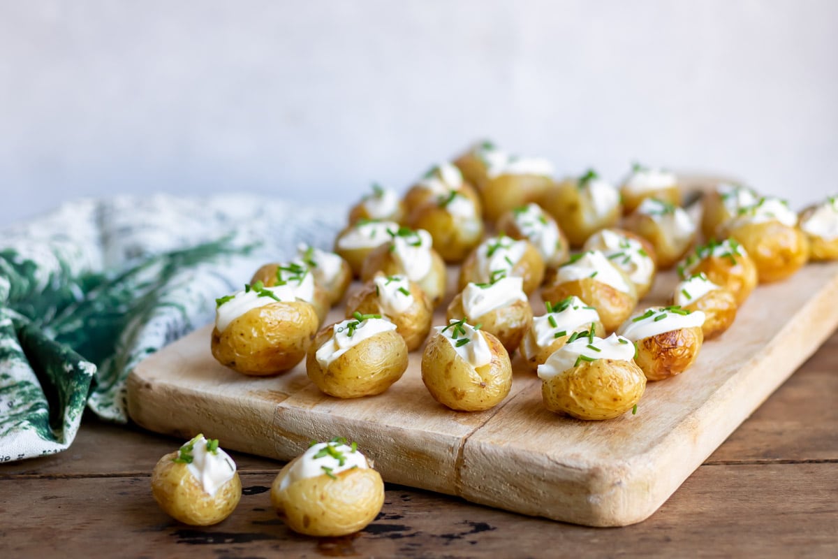 Rows of mini baked potatoes with sour cream on a board.