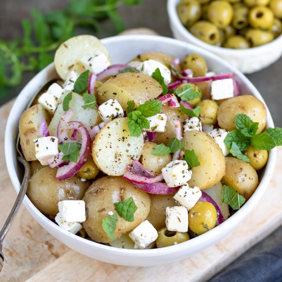 Close up of bowl of potato salad with onion, feta and mint.
