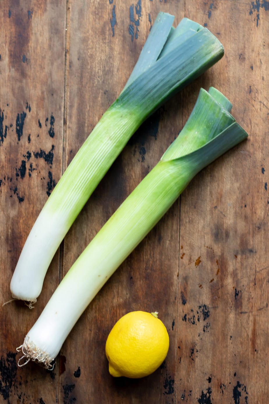 Wooden table with two leeks and a lemon.