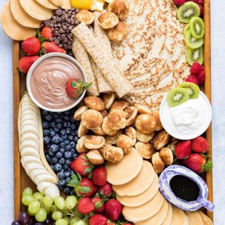 Tray full of pancakes, dip, syrup and fruit.