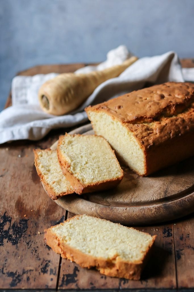 Loaf cake on a wooden board with slices, and a parsnip in the background.