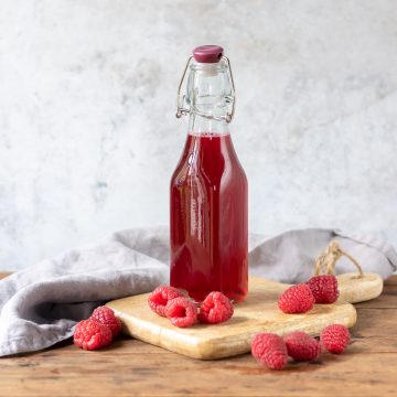 Bottle of raspberry syrup next to raspberries.