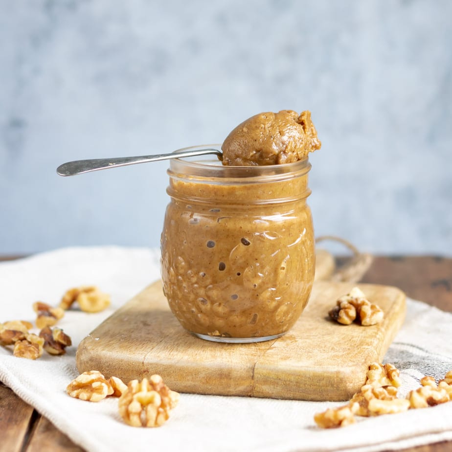 Jar of walnut butter with a spoonful on top.