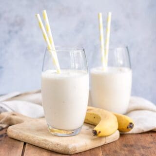 Glasses of banana lassi with straws and bananas next to them.
