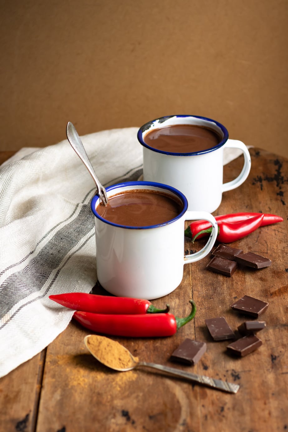 Holztisch mit Tassen Xocolatl, Chili, Zimt und Schokolade.