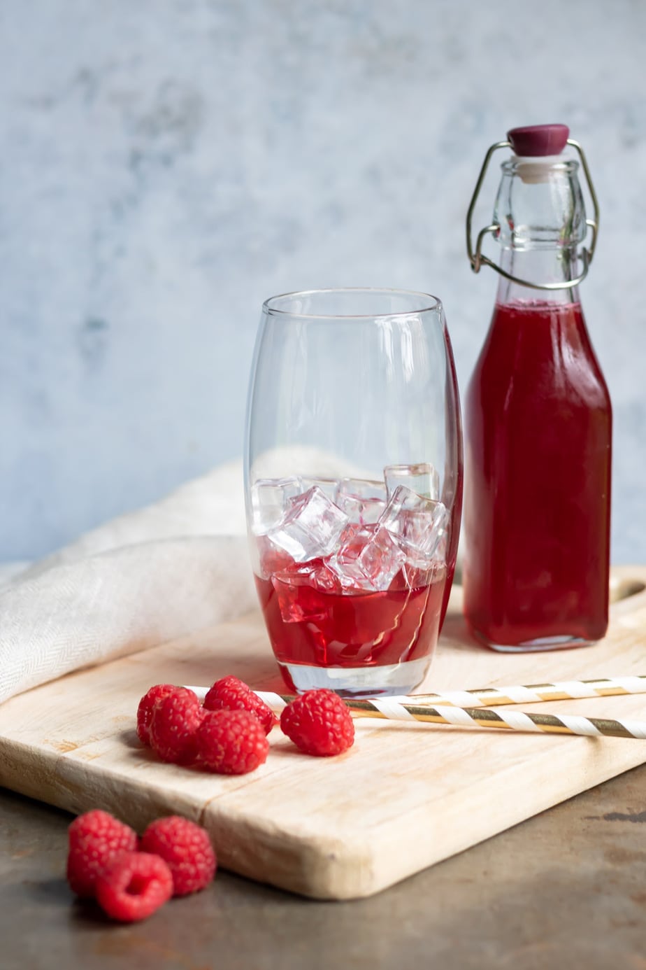 Bottle of raspberry syrup with some in a glass with ice.