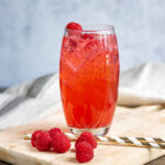 Glass of soda with raspberries and straws.