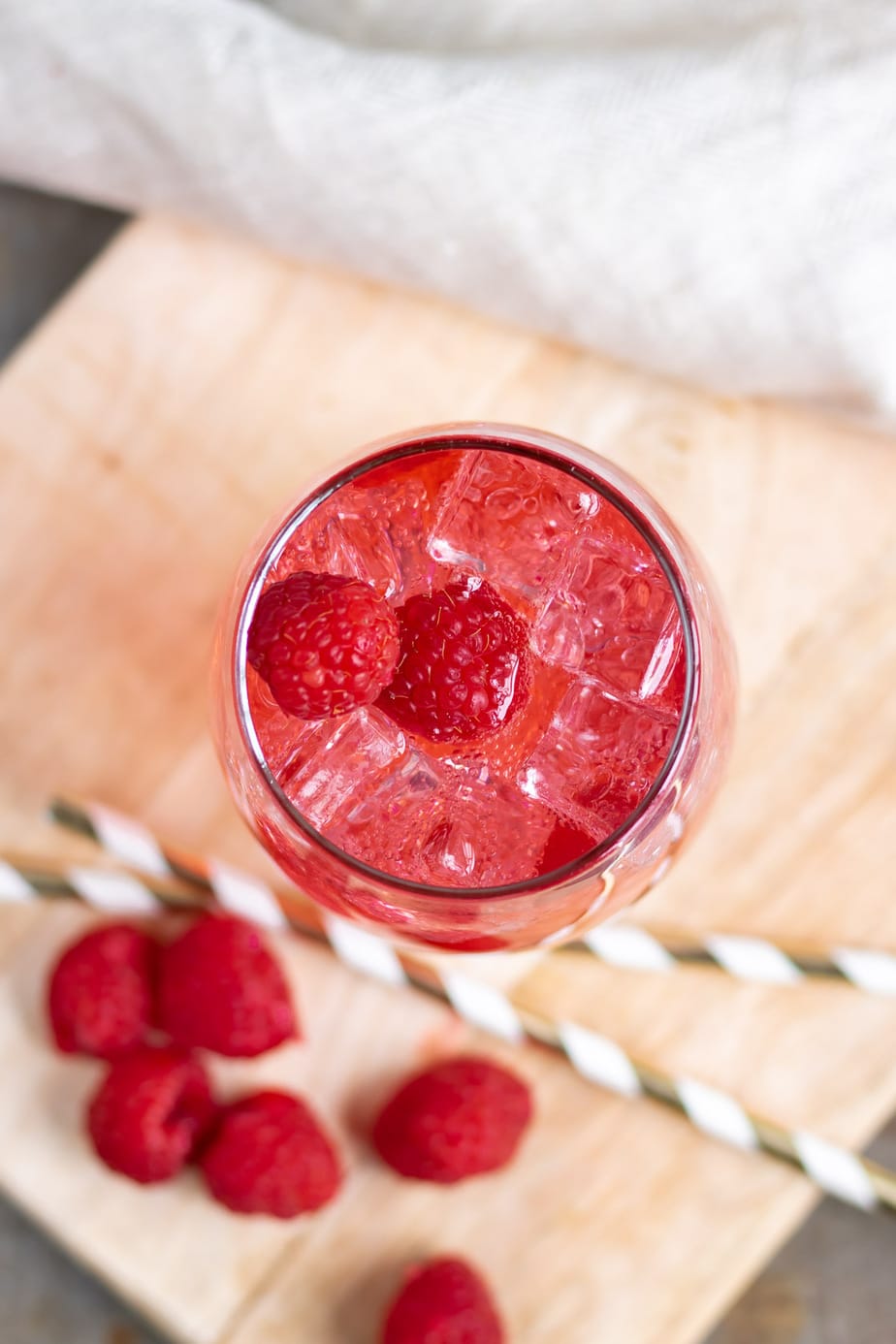 Looking down into a glass of drink with ice and fresh raspberries.