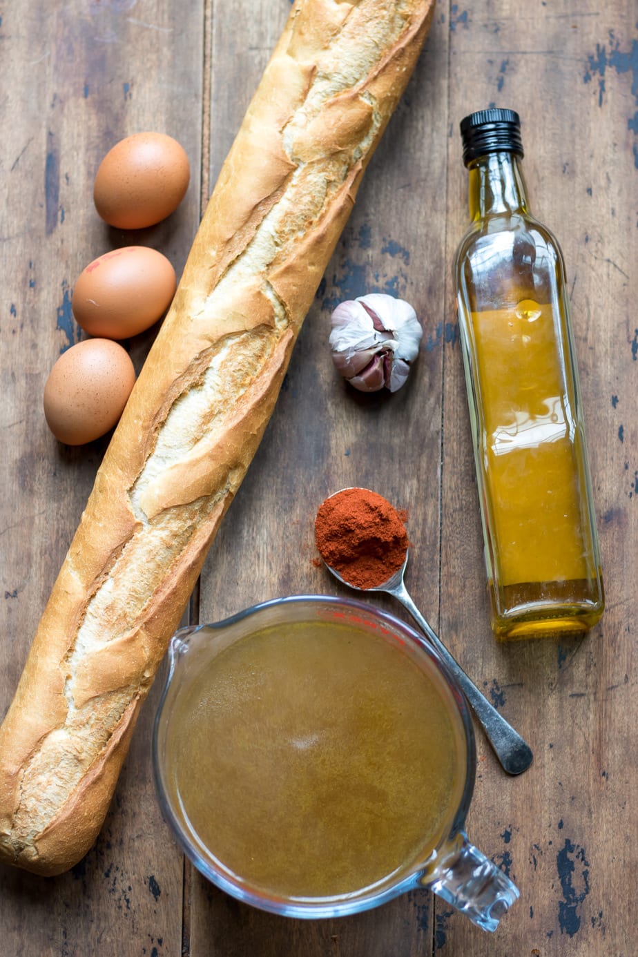 Ingredients on a table: bread, eggs, stock, paprika, garlic and oil.