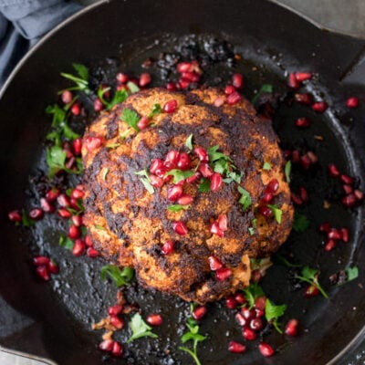 Whole roasted cauliflower in a skillet with pomegranate seeds on top.
