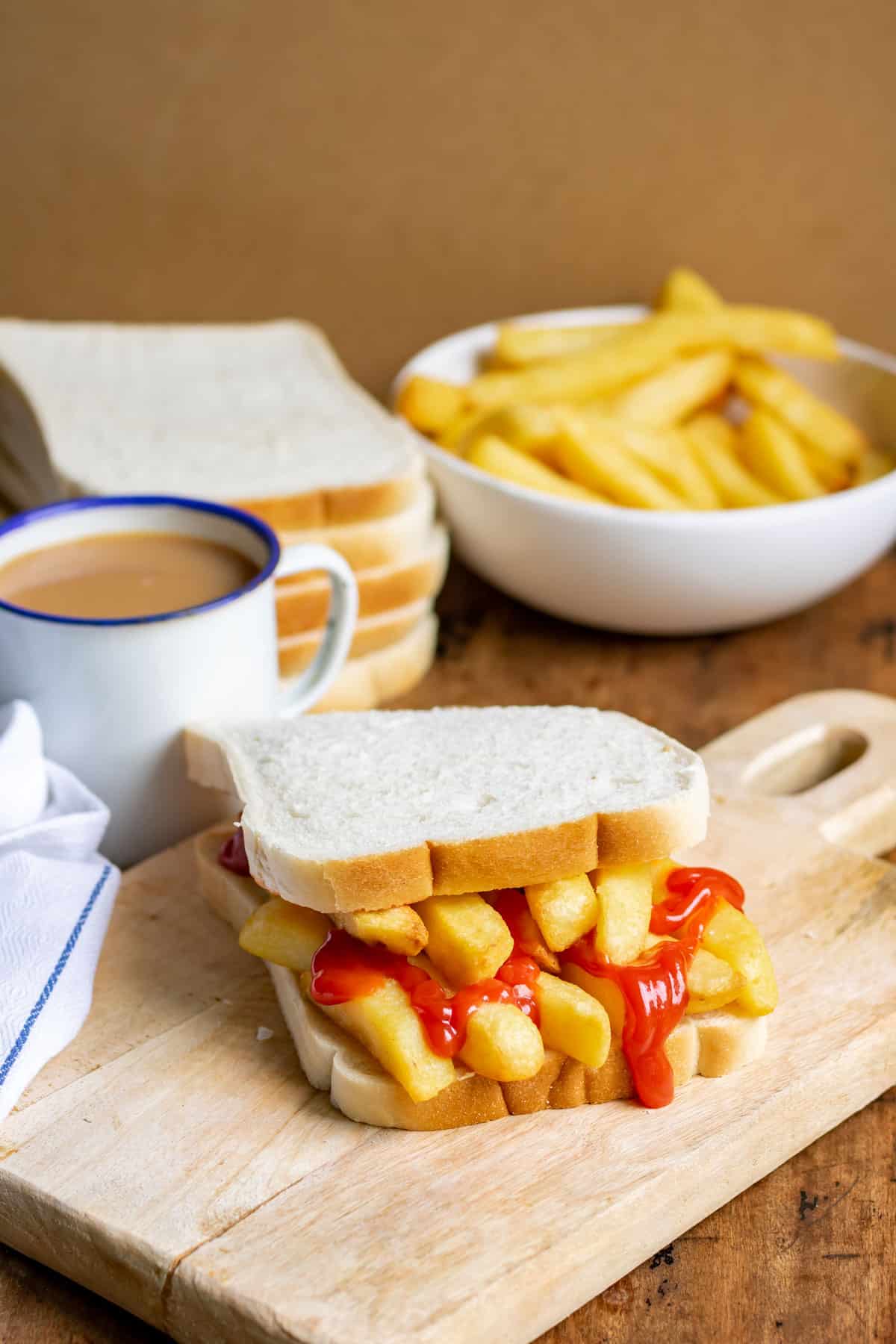 Table with a chip butty, mug of tea, bowl of fries.