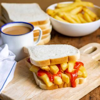 Table with a chip butty, mug of tea, bowl of fries.