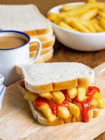 Table with a chip butty, mug of tea, bowl of fries.
