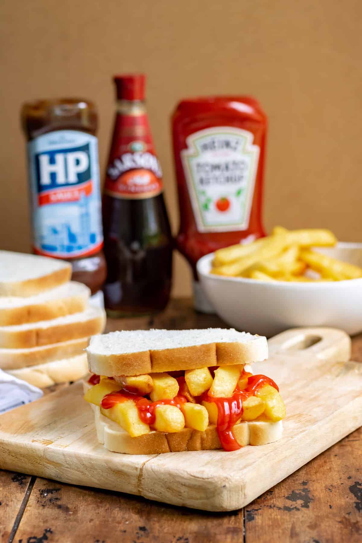 Table with chip butty, bowl of chips, ketchup and HP sauce bottles.