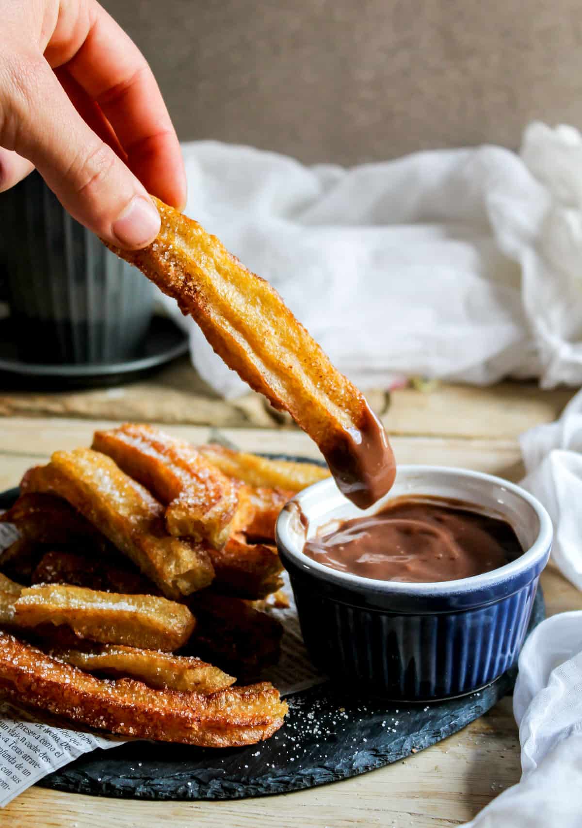 Hand holding a churro coming out of a pot of dipping sauce.
