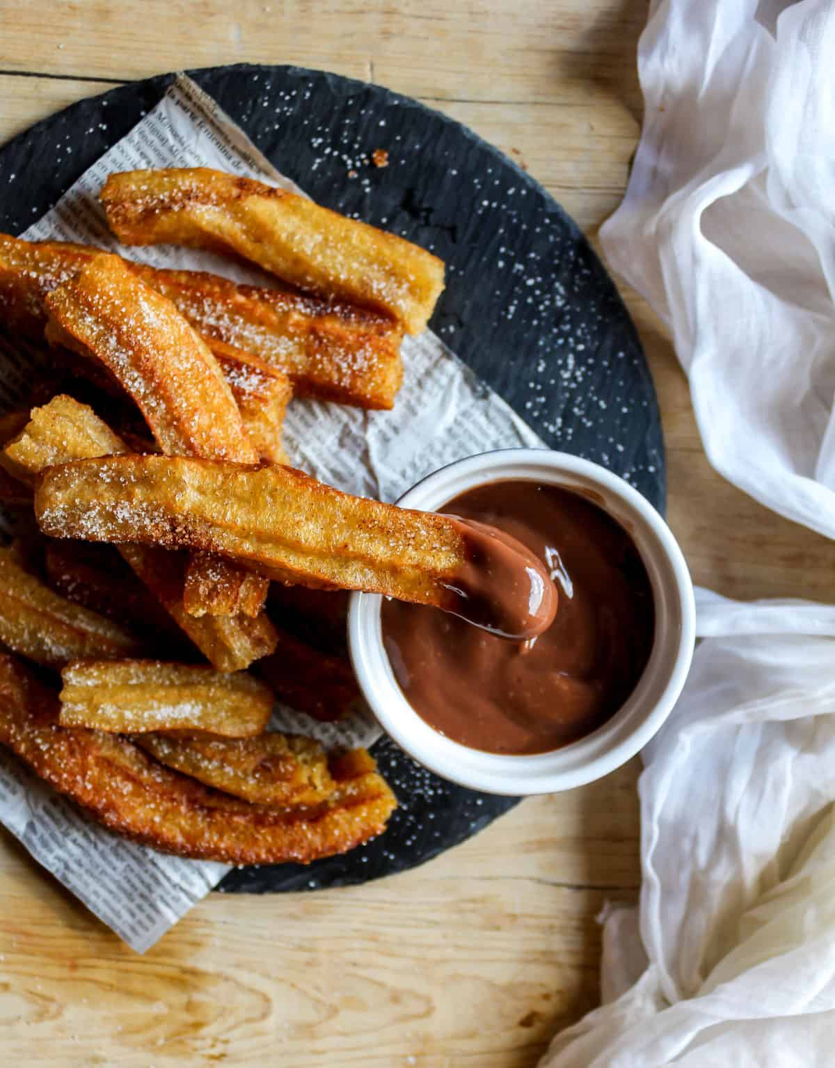 Plate of churros with one in chocolate sauce.
