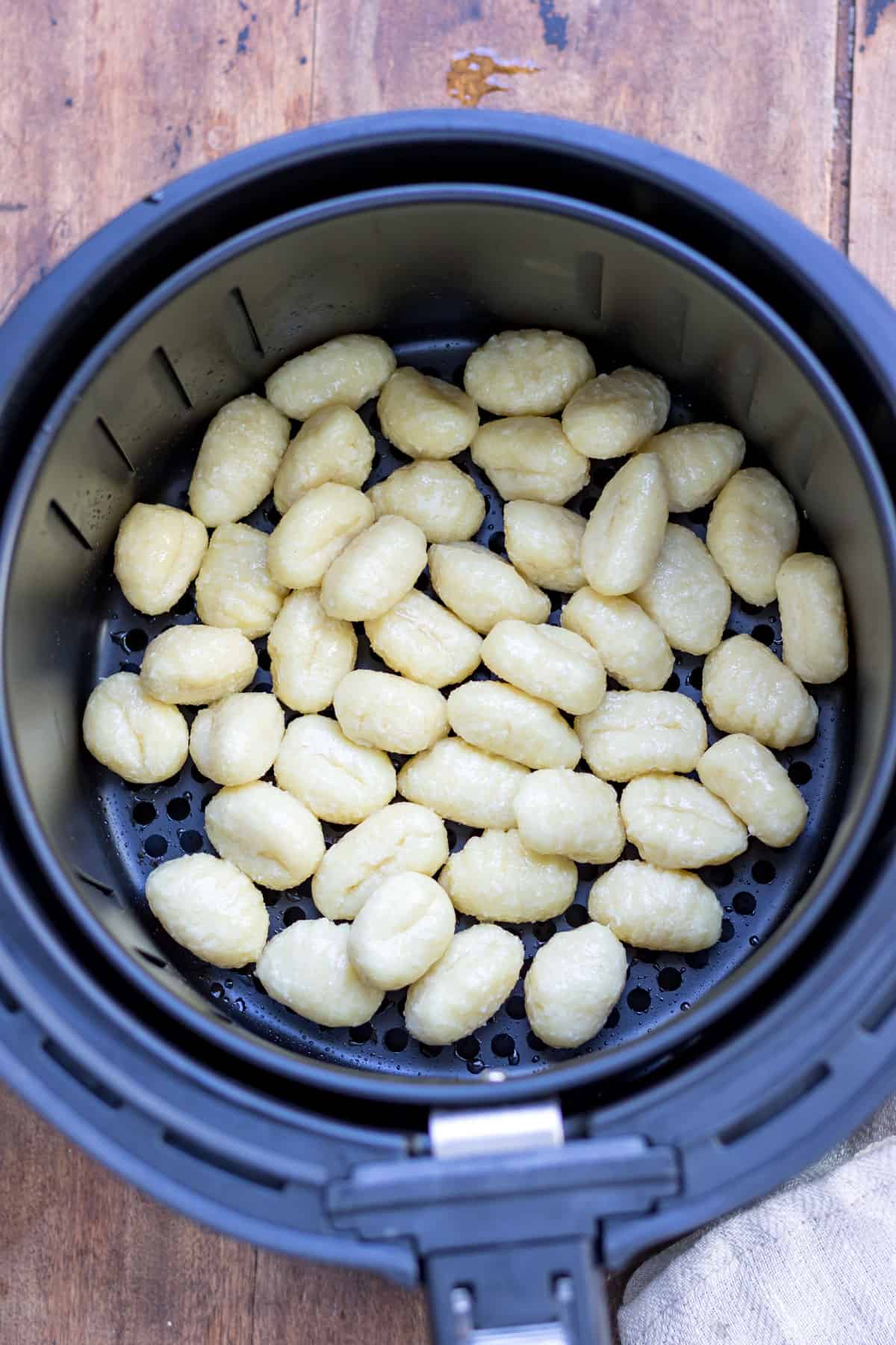 Uncooked gnocchi in an air fryer basket.