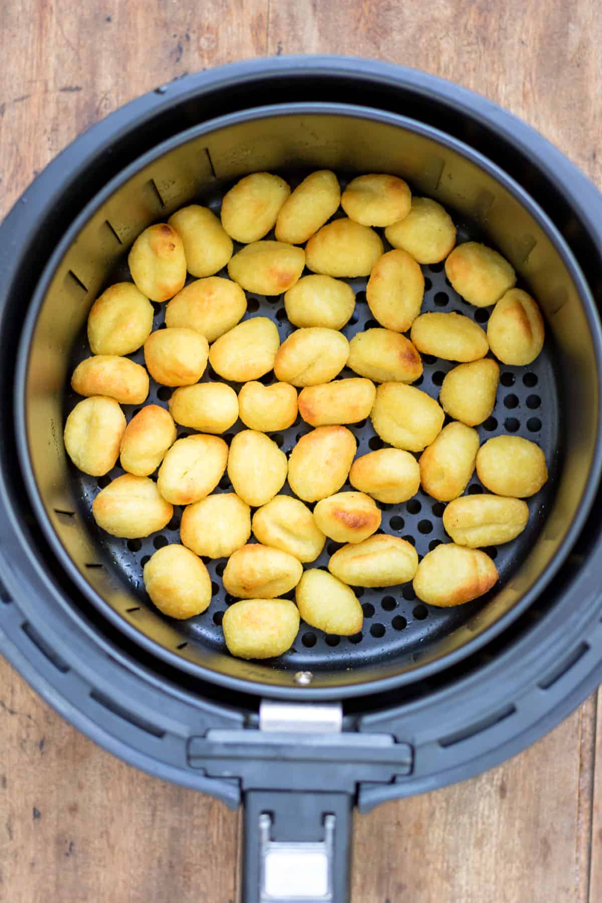 Cooked gnocchi in air fryer basket.