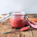 Jar of rhubarb sauce on a wooden table.