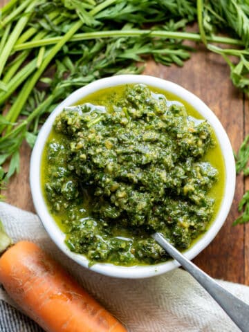 Small bowl of pesto on a table next to a bunch of carrots.