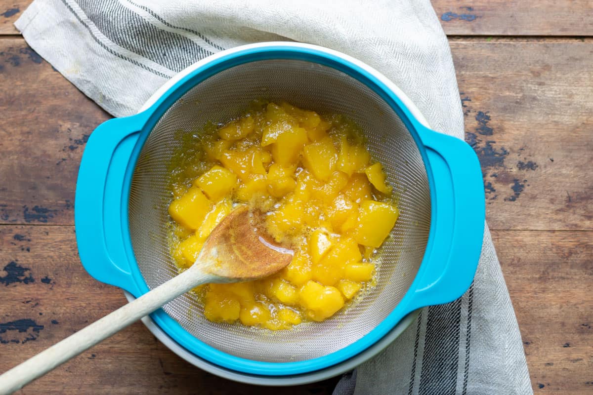 Straining mango syrup into a bowl.