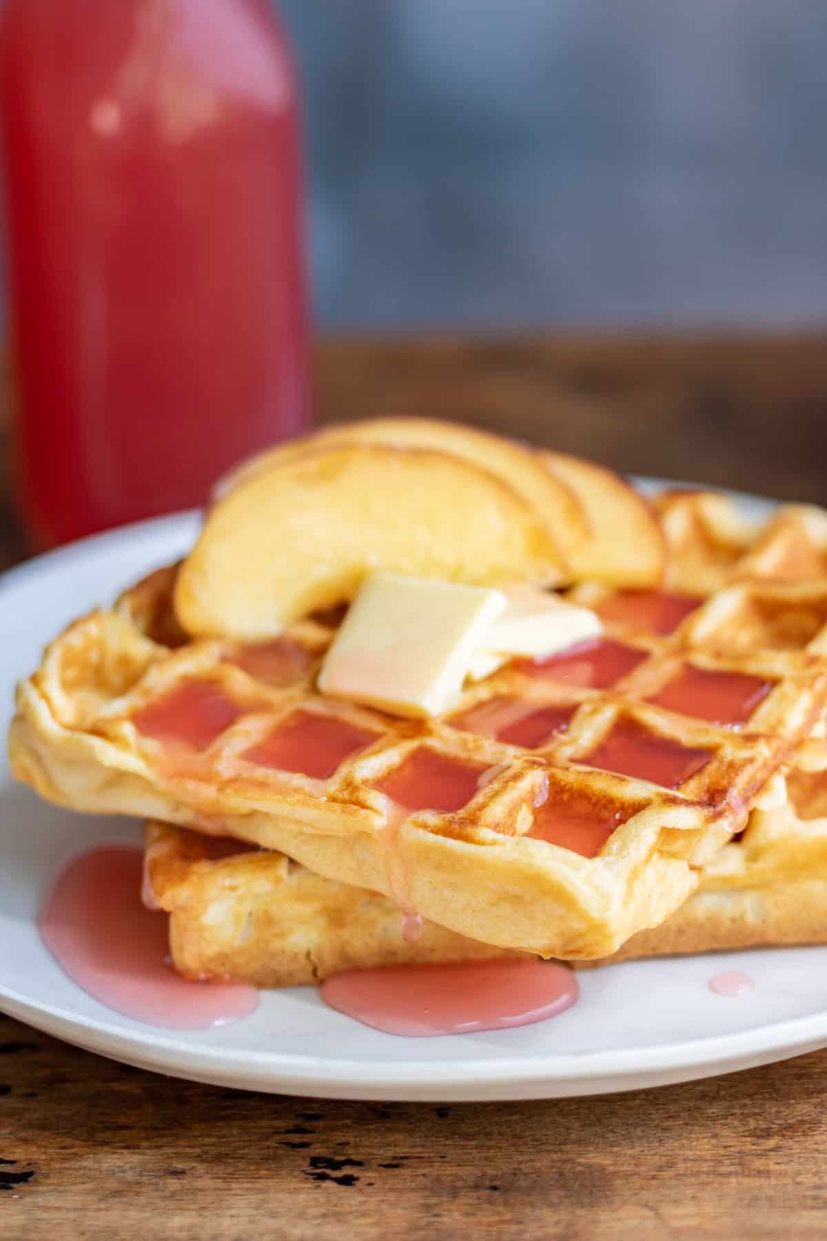 Waffles with butter, sliced peaches and peach syrup.