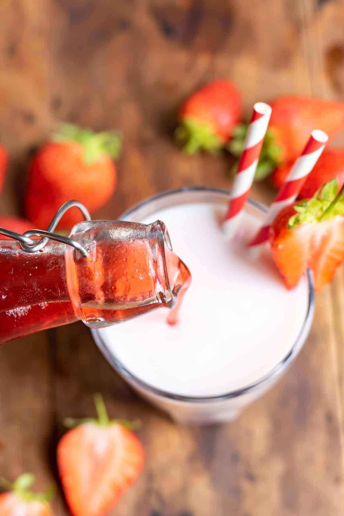 Strawberry syrup being poured into a glass of milk.